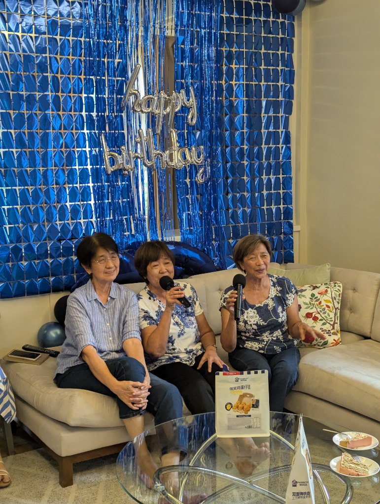 Three sisters singing on the couch with microphones in front of the happy birthday backdrop